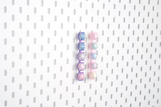 Two five-piece pegboard bobbin holder sets in violet purple and pink, storing ten sewing bobbins