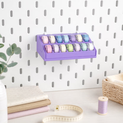 Bobbin organizer mounted above a sewing workspace with fabric and measuring tape