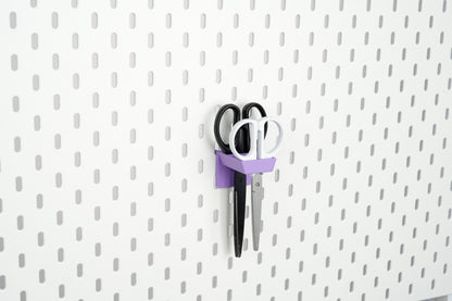 Purple three-slot pegboard scissors holder storing two pairs of scissors on IKEA SKÅDIS